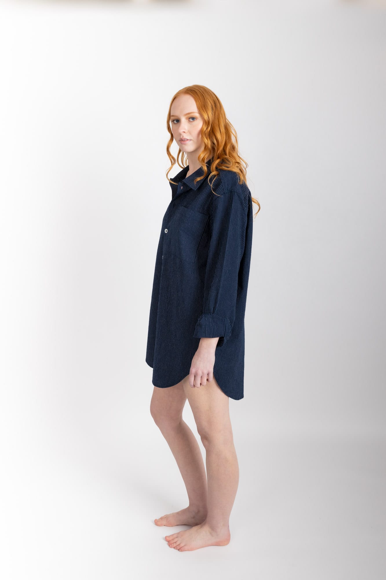 A classic man style shirt silhouette, lengthened, with a rounded hem and buttoned cuff. Featuring a single breast pocket, back box pleat and locker loop detail, and natural shell buttons.  In navy pinstripe,  and woven in 100% organic cotton , this shirt is finished with French seams.