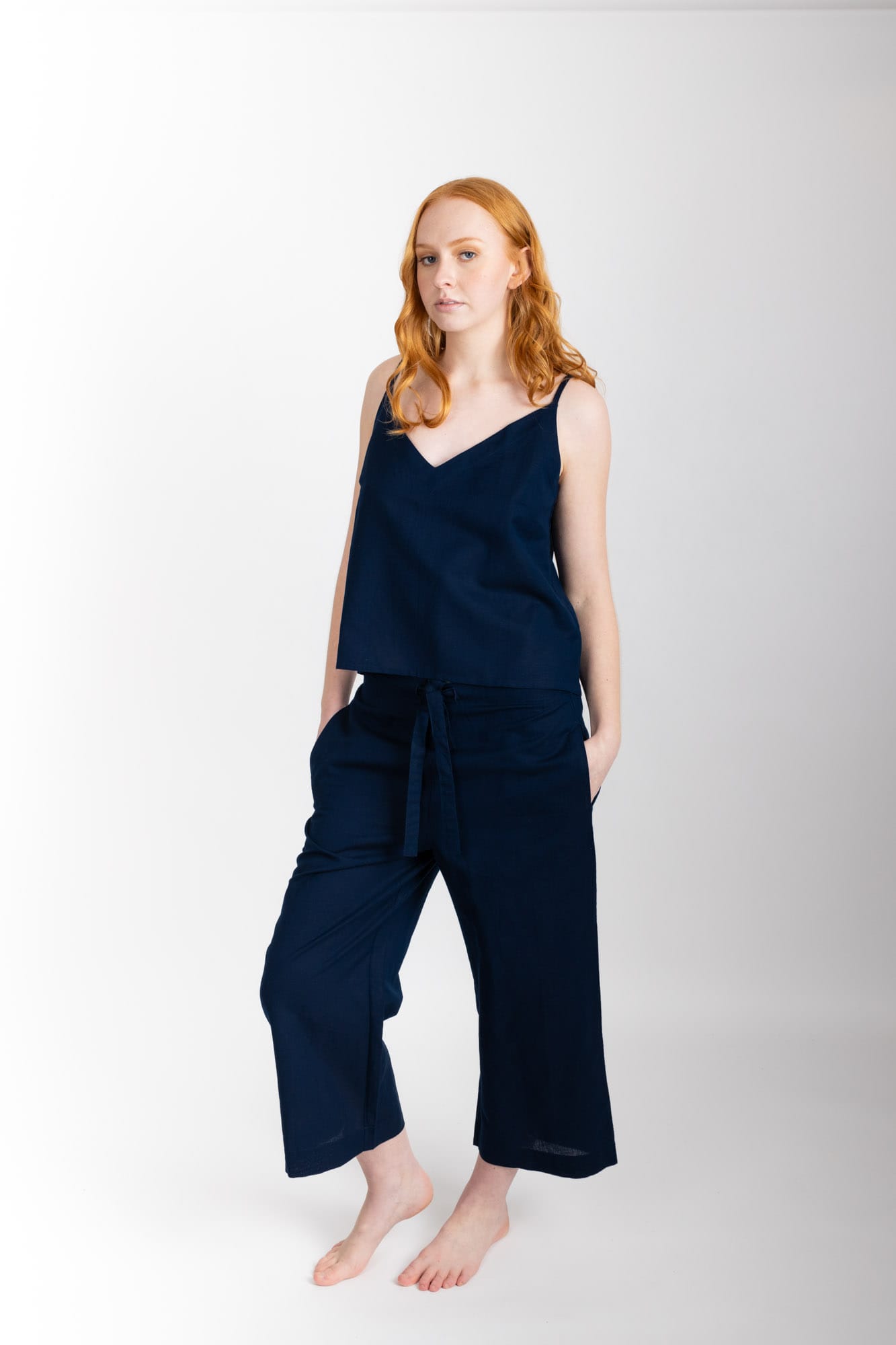 Women’s sleepwear set featuring a V-neck, swing-style camisole with adjustable straps. Paired with straight-leg cropped pant with an elasticated waist, flat front, and drawstring detail, these pants are comfortable and flattering. Woven in 100% organic cotton, both pieces have been finished with French seams.