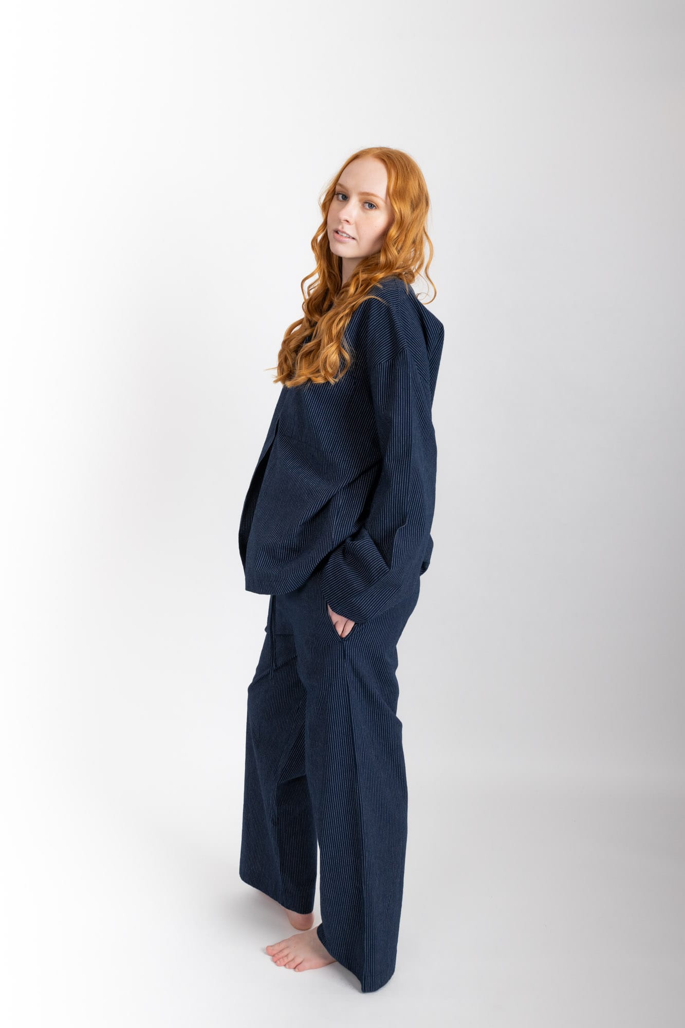 Women’s sleepwear set featuring an oversized, dropped-shoulder, button-through shirt, with natural shell buttons.  The loose-fit, straight-leg pants have an elasticated waist, flat front, and drawstring detail, and are comfortable and flattering. Made from 100% organic cotton in Navy Pinstripe, both pieces have been finished with French seams.