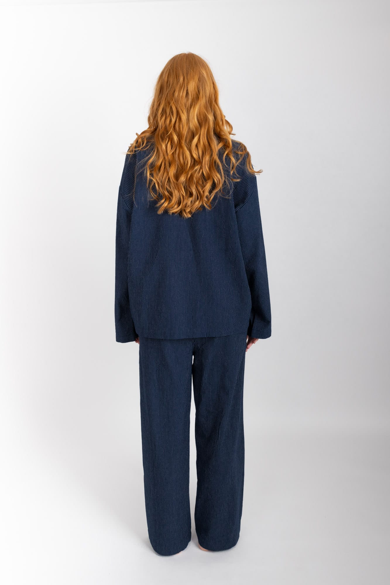 Women’s sleepwear set featuring an oversized, dropped-shoulder, button-through shirt, with natural shell buttons.  The loose-fit, straight-leg pants have an elasticated waist, flat front, and drawstring detail, and are comfortable and flattering. Made from 100% organic cotton in Navy Pinstripe, both pieces have been finished with French seams.